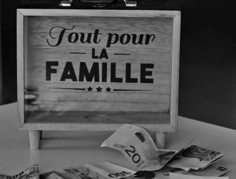 Black and white photo of a money box and various currencies on a table, symbolizing savings for family.