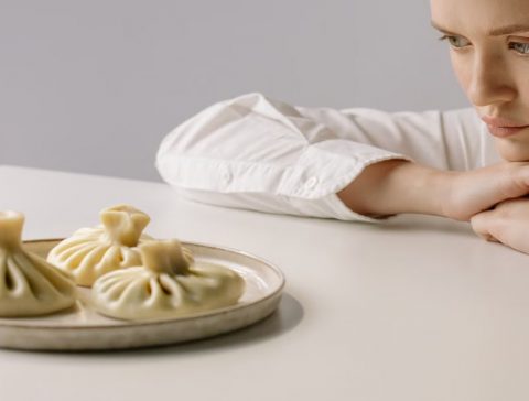 A woman in a white shirt gazes at a plate of traditional Georgian khinkali dumplings.