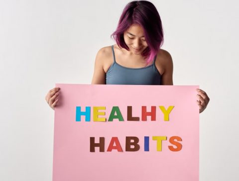 Asian woman holding a colorful 'Healthy Habits' sign in a studio setting, promoting wellness.